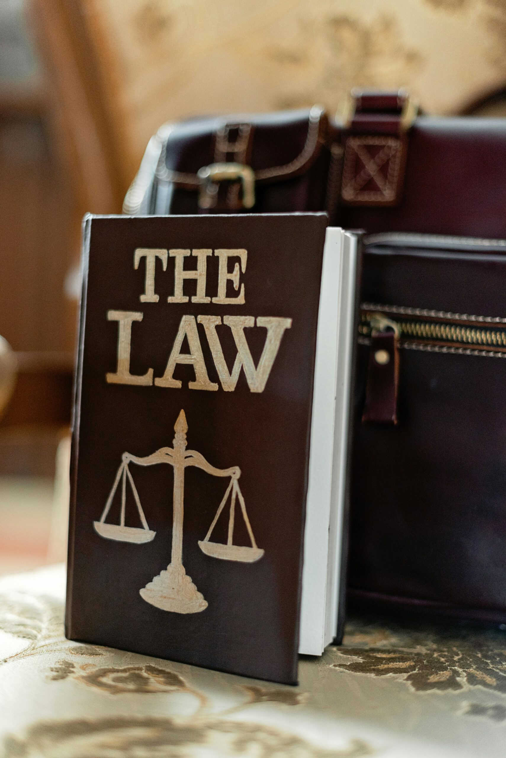 Law book titled “The Law” with scales of justice beside a leather briefcase