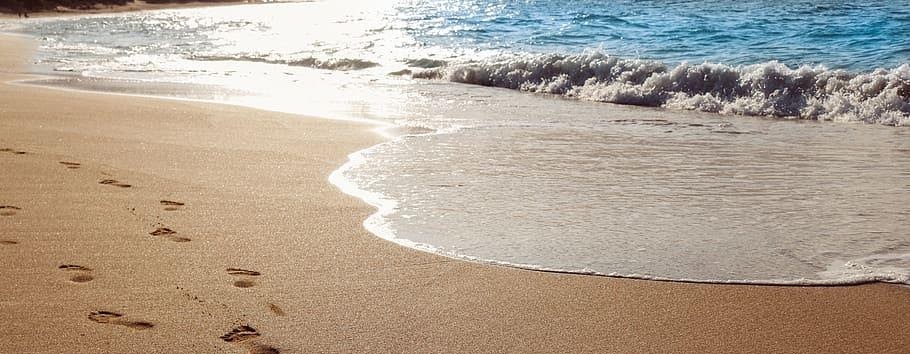 Footprints in the sand leading along a beach with ocean waves.