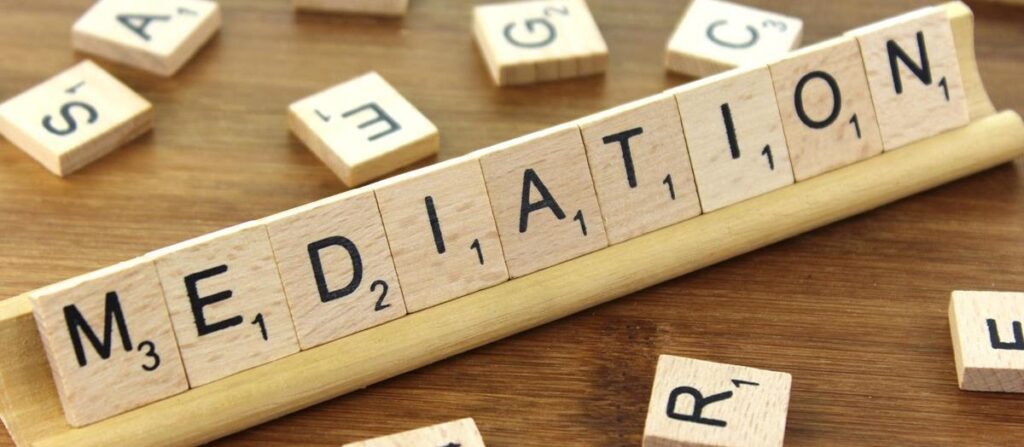 Scrabble tiles spelling out the word MEDIATION on a wooden surface.