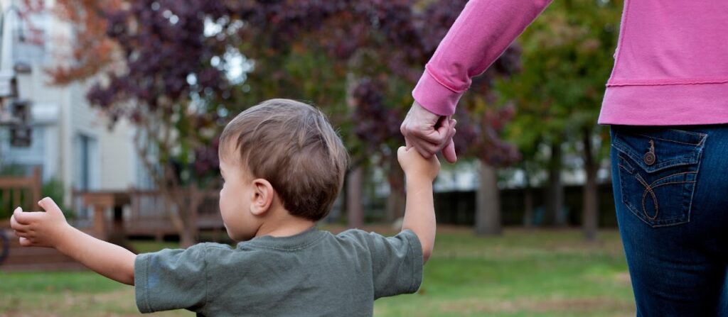 Close-up of a toddler holding an adult's hand while walking outdoors.