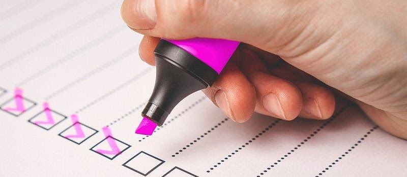 Hand using a pink highlighter to check off boxes on a legal document or checklist.