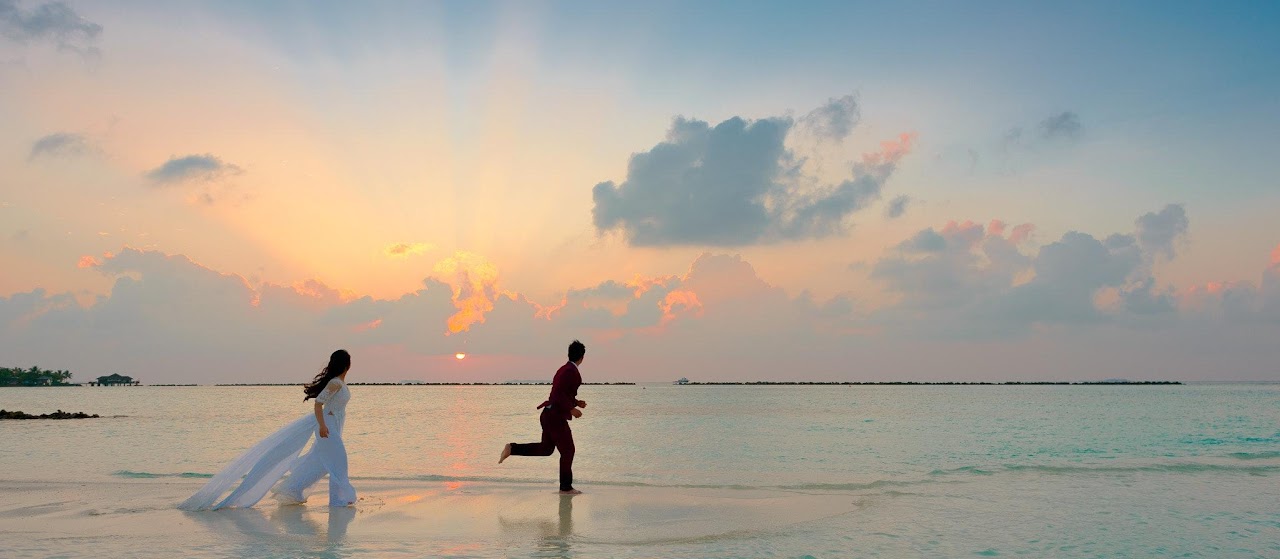 Bride and groom running on a sandy beach at sunset.