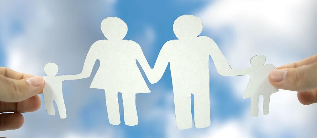 Paper cutouts of a family being held together by hands against a blue background.