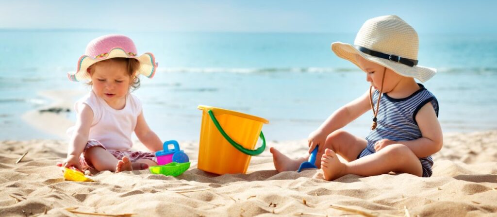 Two young toddlers playing with sand toys on a sunny beach.